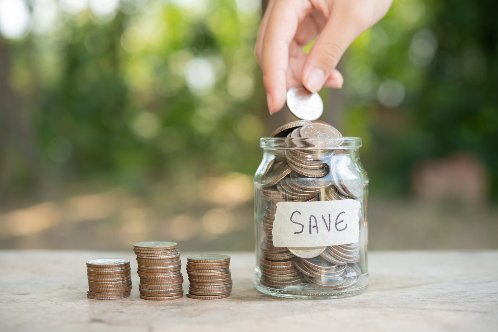 Three stacks of coins next to a glass jar of coins