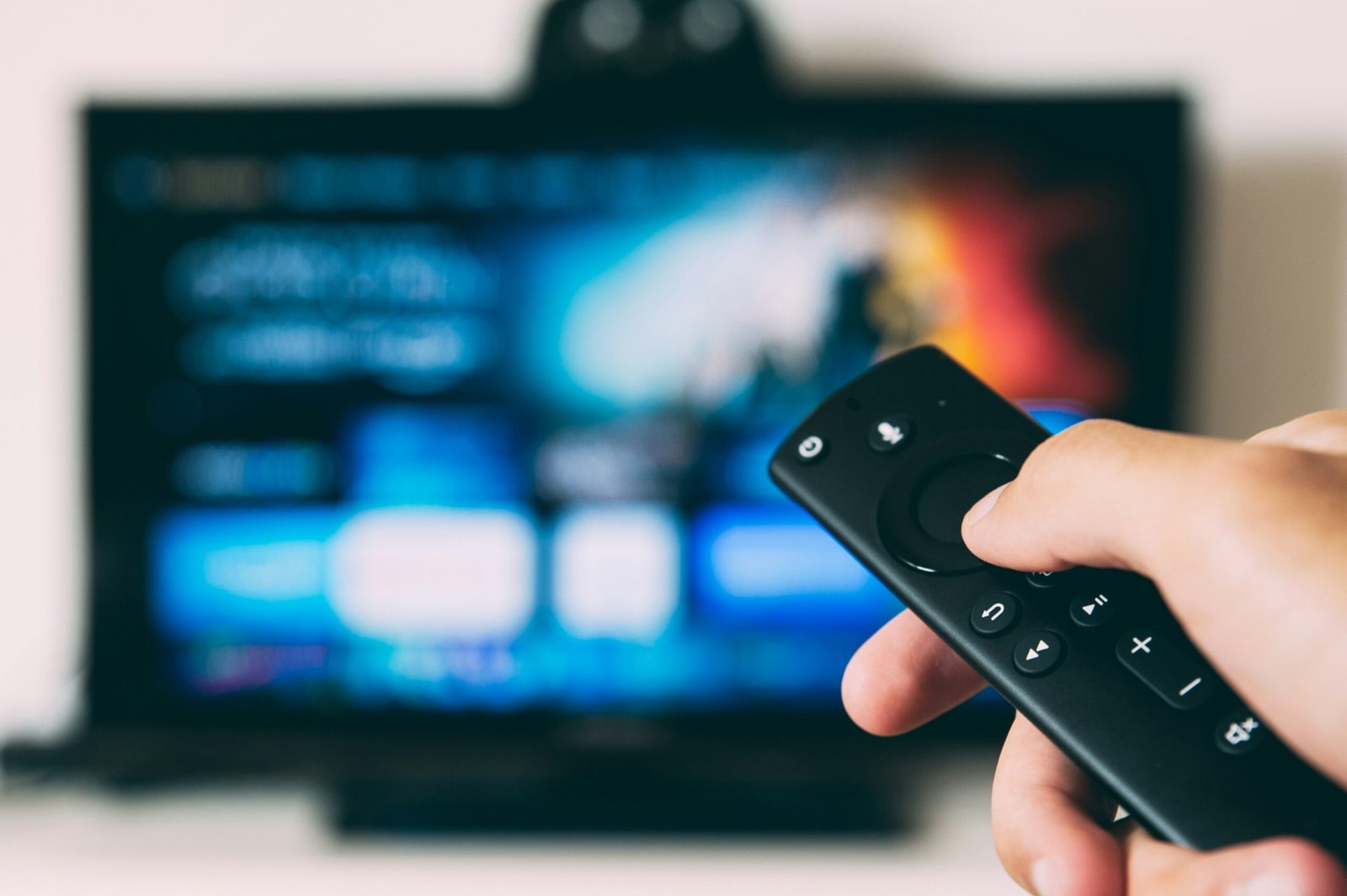 IMAGE: Hand holding a remote in front of a Television. glenn-carstens-peters-EOQhsfFBhRk-unsplash